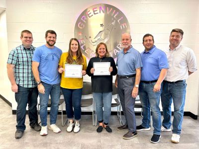 seven persons stand in one line in front of a cinderblock wall and Greenville Elementary metallic seal